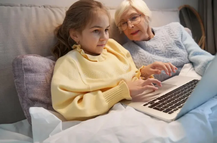 grandmother and granddaughter sitting in bed looking at a computer