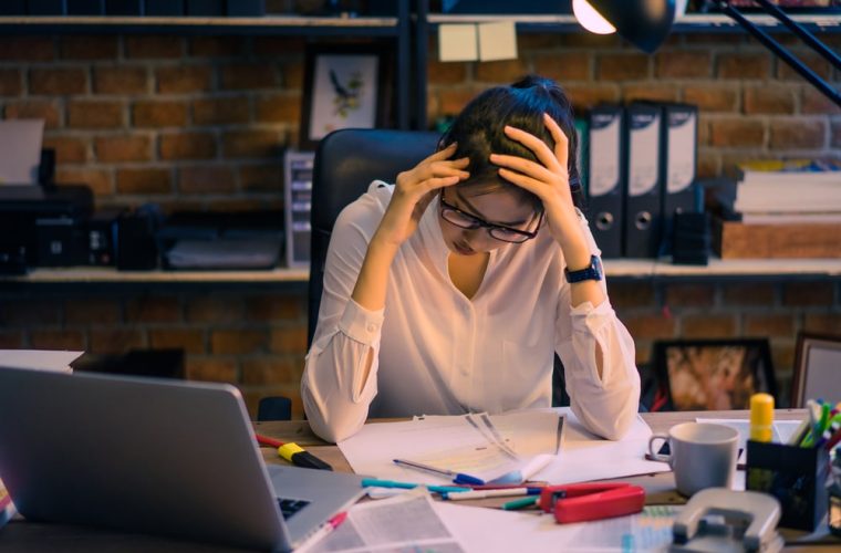 worried woman holding her head at an office desk